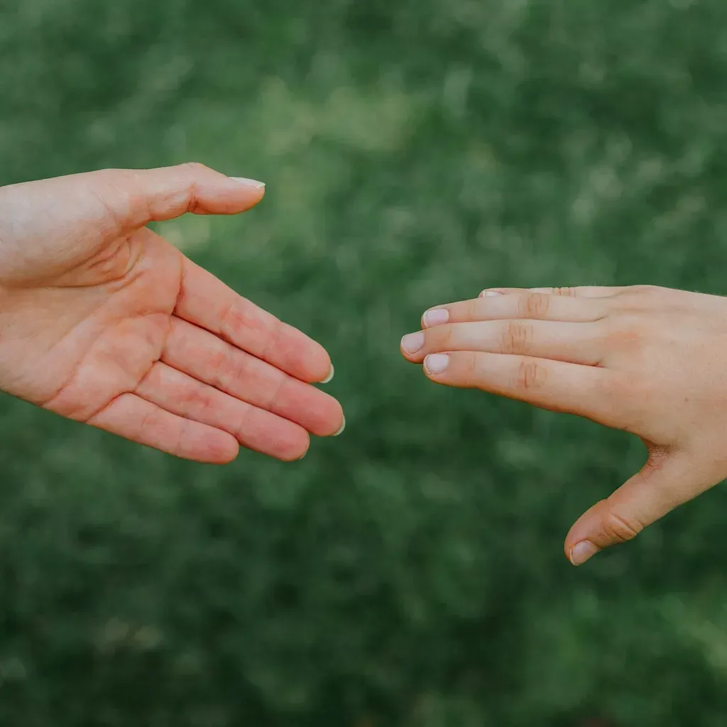 Two open hands reaching towards each other against green grass