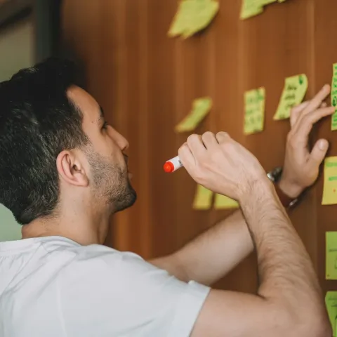 A man writing on green sticky notes stuck to a timber wall