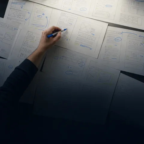 A hand sketching page wireframes across overlapping sheets of paper